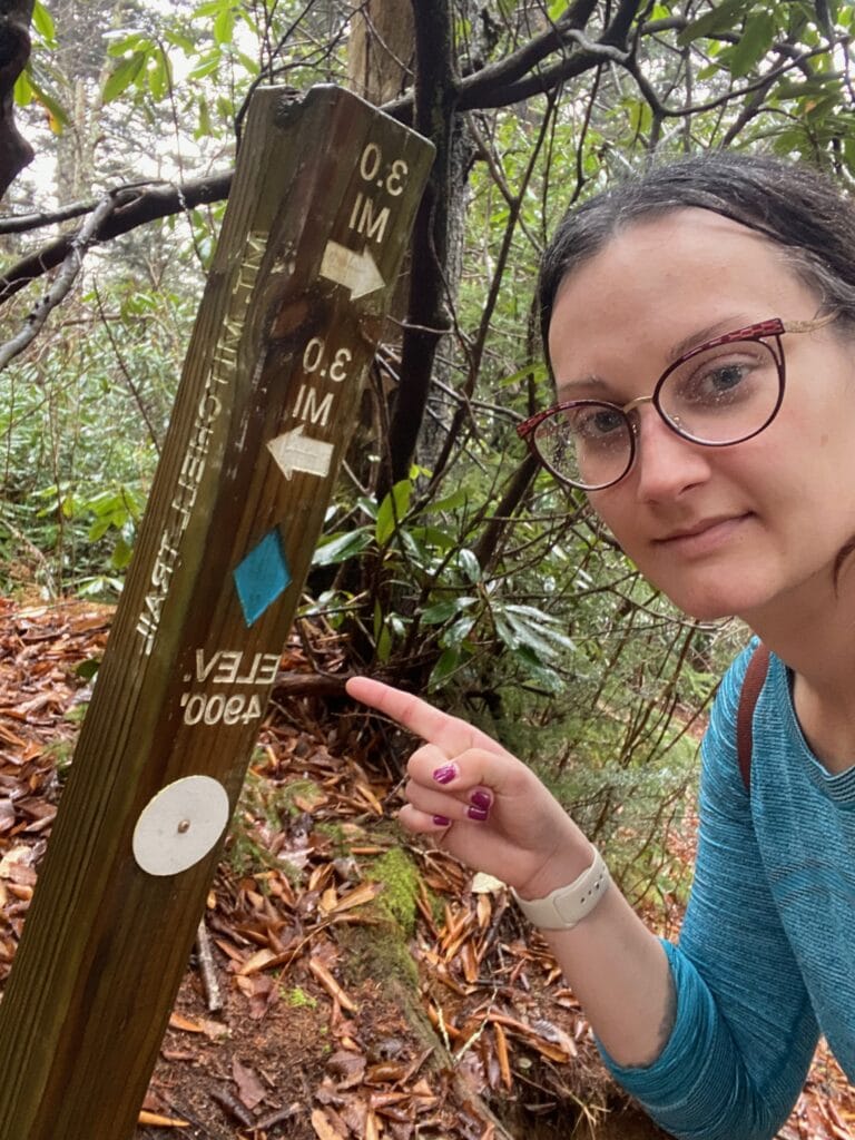 Woman posing with halfway marker on Mt. Mitchell Trail.