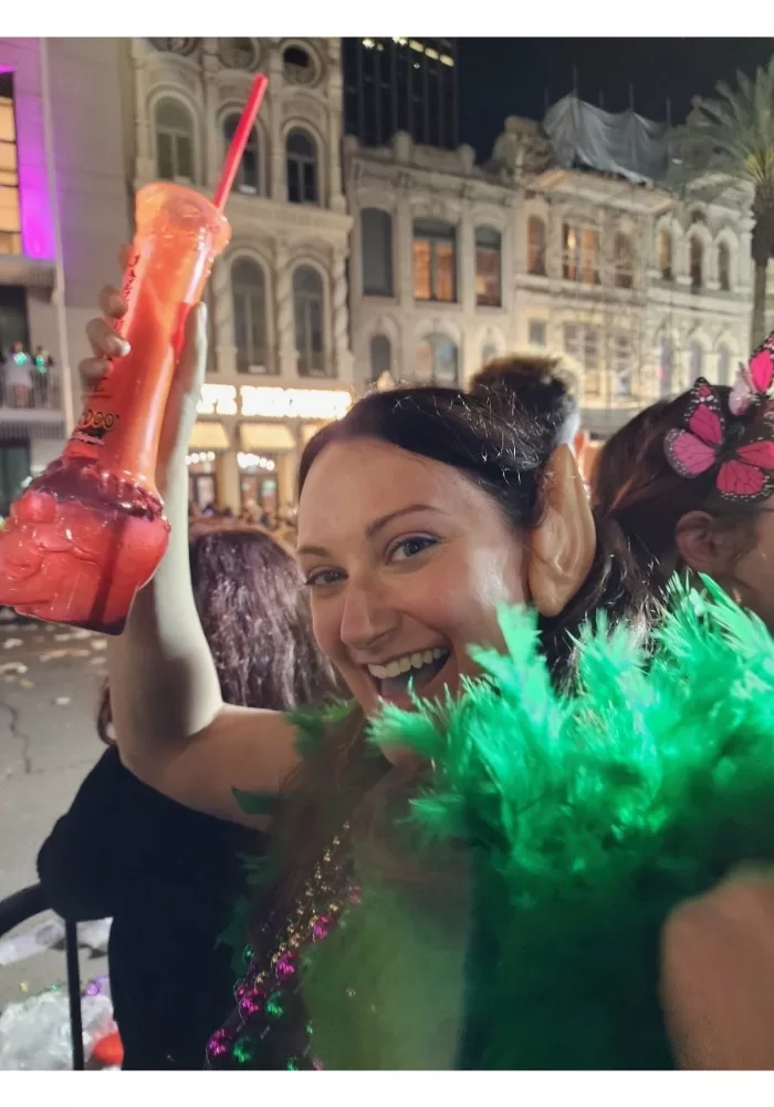 Woman with elf ears and green boa holding orange alcoholic drink at Mardi Gras