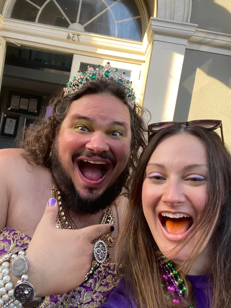 Street performer man wearing crown and dress posing with woman attending Mari Gras