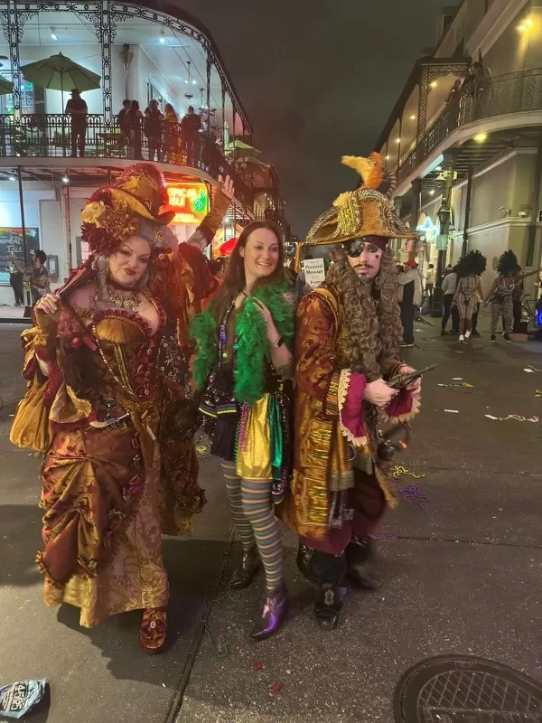 Two people dressed in pirate costumes posing with a woman in the middle on Bourbon Street at Mardi Gras