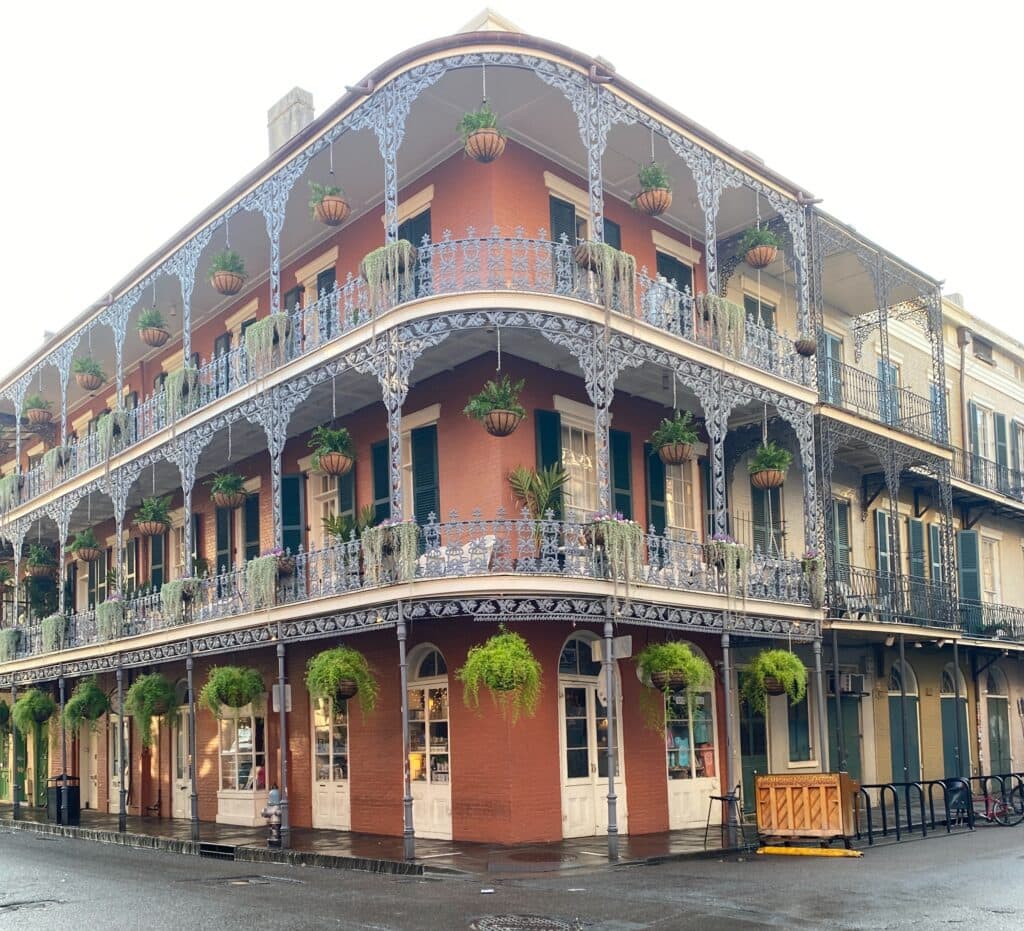 famous balcony on Royal Street in New Orleans. Plants overhang on the balconies of a 3 story brick building.