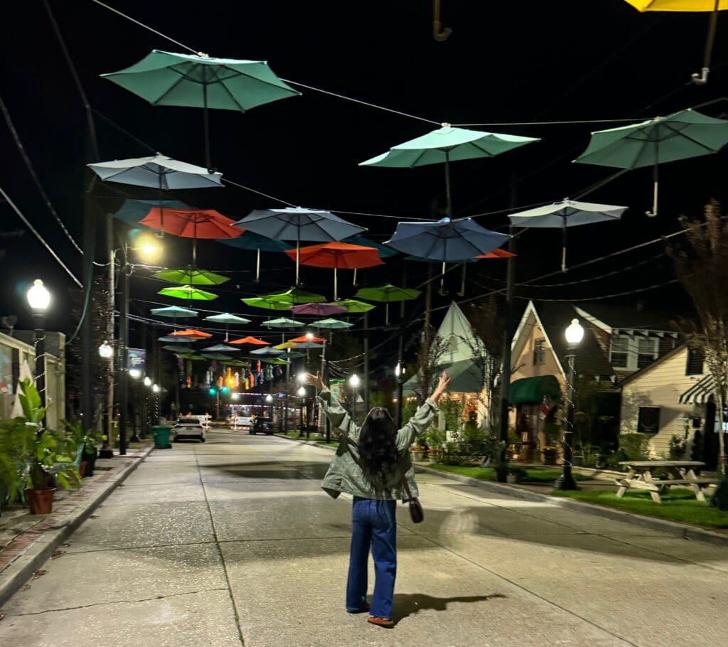 woman standing beneath colorful umbrellas hanging from a clothesline at night