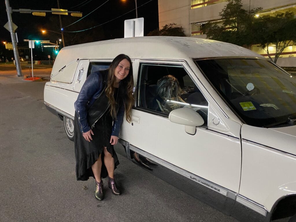 woman posing by white hearse with skeleton inside