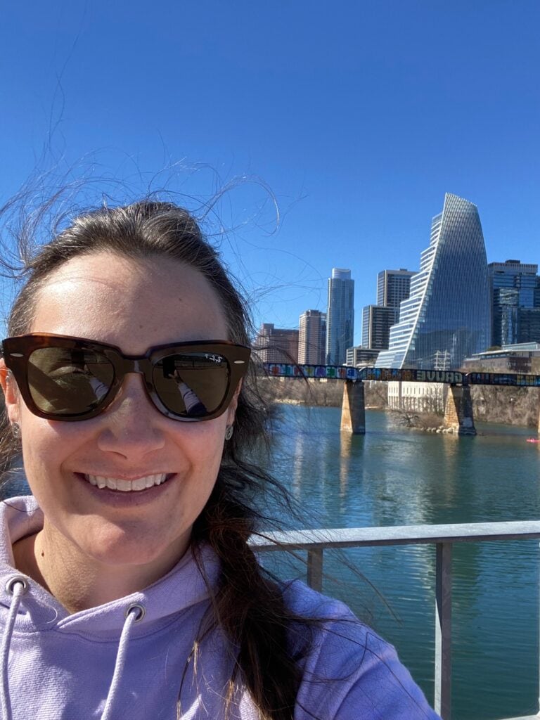 woman posing in front of Lady Bird Lake with austin skyline in the background