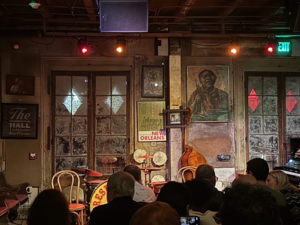 A dimly lit jazz club stage in New Orleans with vintage instruments and wooden chairs offers a cozy, rustic atmosphere—one of the best things to do alone in New Orleans as you soak up the warm lights and wait for an unforgettable performance.