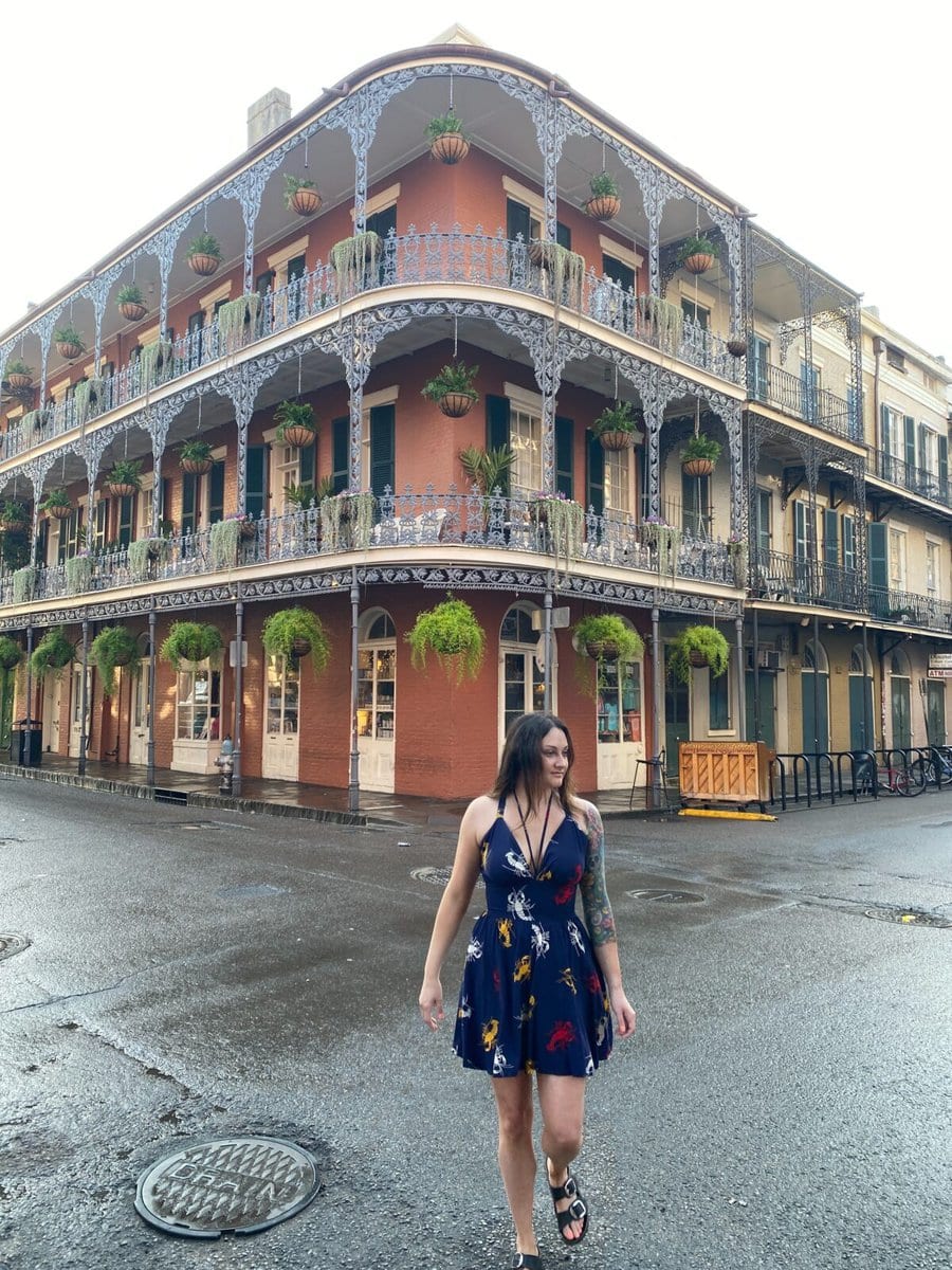 Woman crossing the street. Famous pink building with decorated balcony on Royal Street is in the background. One of many things to do alone in New Orleans