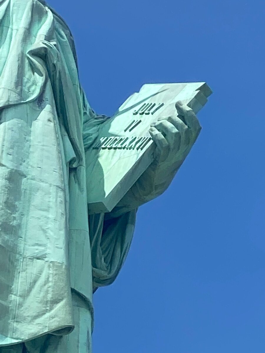 Close-up of the Statue of Liberty’s hand holding a tablet inscribed with JULY IV MDCCLXXVI against a clear blue sky—a must-see for any solo female travel NYC adventure.