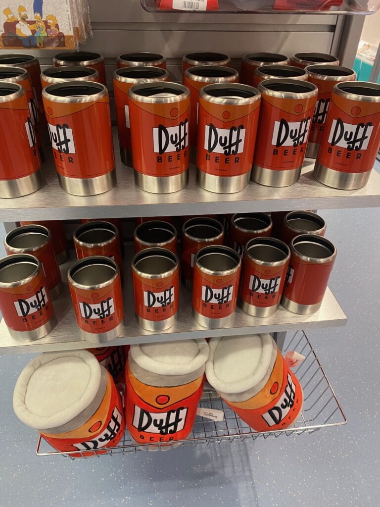 Several shelves display red Duff Beer cans and cup holders, with a wire rack below holding plush Duff Beer hats—all themed after the fictional brand from The Simpsons. It’s a quirky find for fans seeking unique things to do alone in Myrtle Beach.