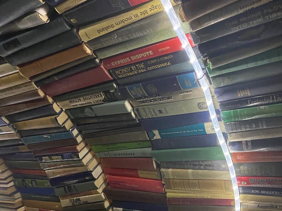 A tunnel-like arch made of stacked books, with a strip of bright LED lights running along the curve, illuminating the book spines in various colors and titles.