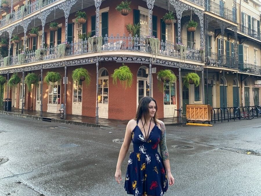 Woman crossing the street. Famous pink building with decorated balcony on Royal Street is in the background. One of many things to do alone in New Orleans