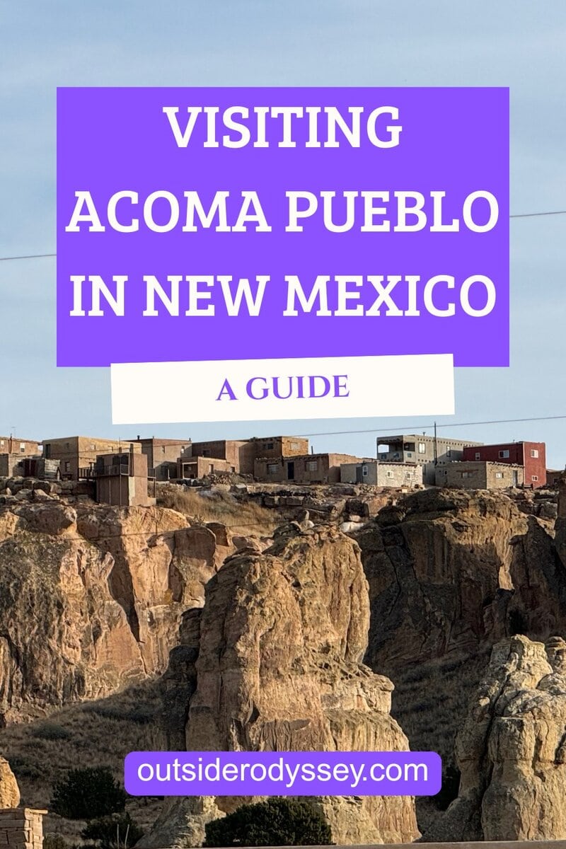 Rocky desert cliffs with adobe buildings perched on top under a clear sky. Overlaid text reads: Visiting Acoma Pueblo in New Mexico. A Guide for those interested in visiting Acoma Pueblo. outsiderodyssey.com.