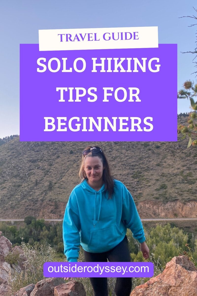 A woman in a blue hoodie hikes on rocky terrain with hills in the background. Overlaid text reads: Travel Guide: Solo Hiking Tips for Beginners, featuring essential solo hiking tips at outsiderodyssey.com.