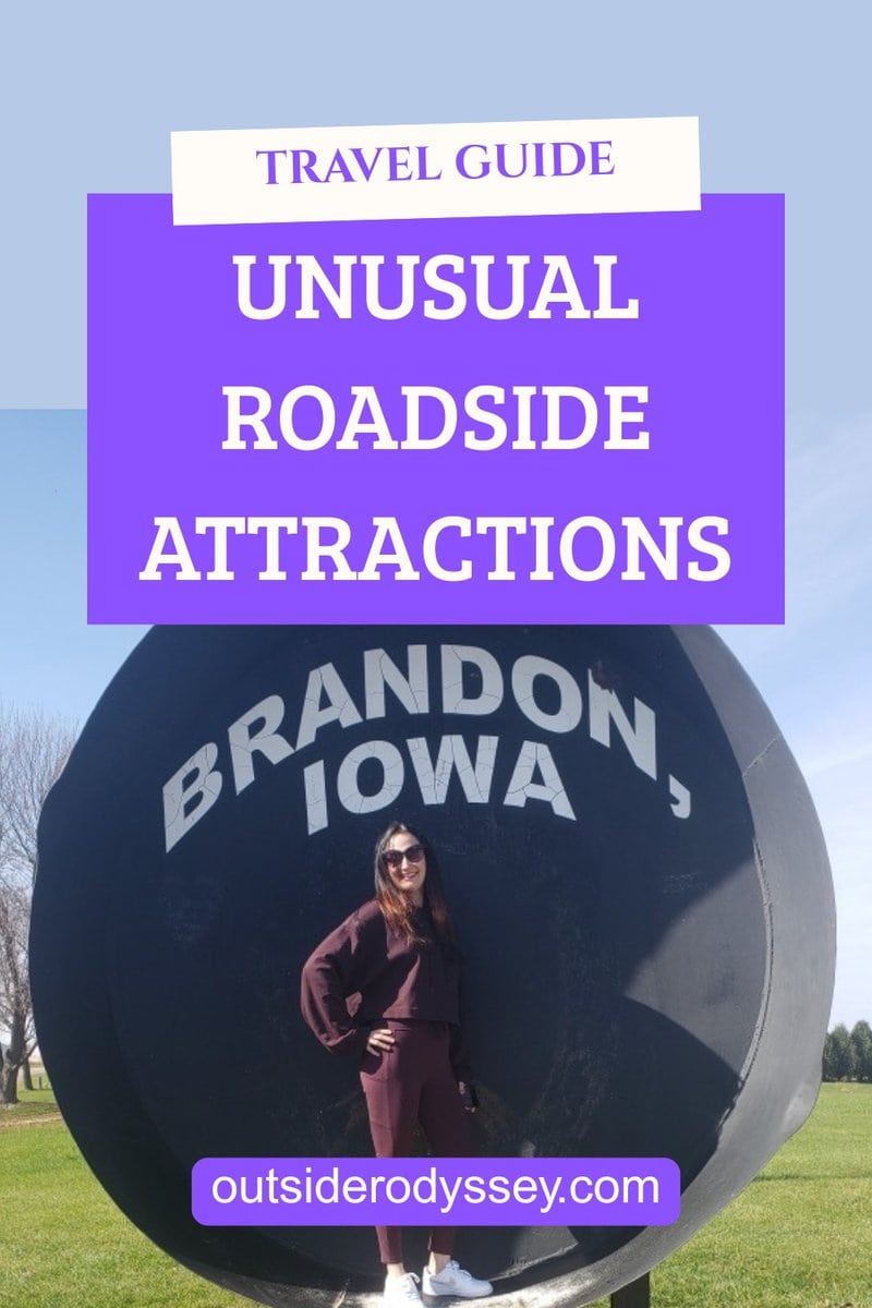 A woman in sunglasses stands in front of a large black sign reading Brandon, Iowa under bright blue sky. Text overlays above her read Travel Guide: Unusual Roadside Attractions and outsiderodyssey.com.