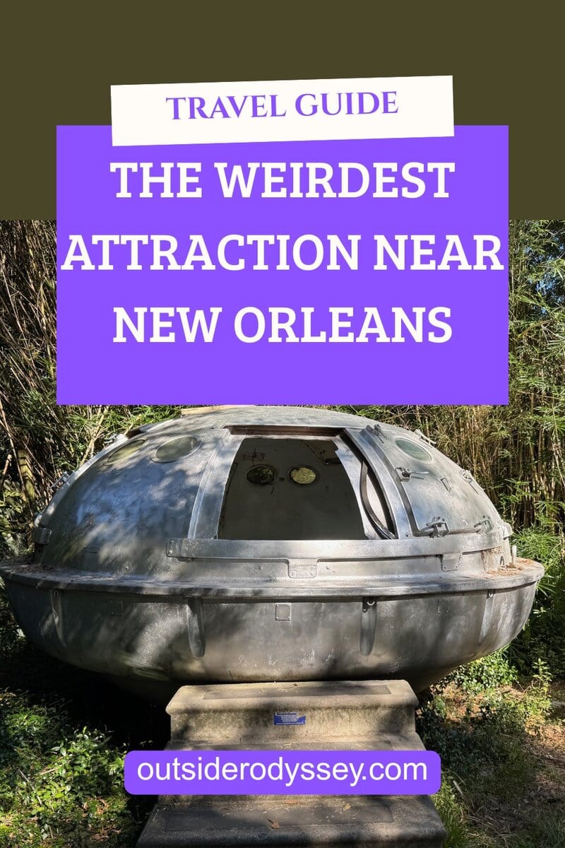A round, metallic, UFO-like structure with a small door and dials sits outdoors among trees at the Abita Mystery House. Text reads: Travel Guide: The Weirdest Attraction Near New Orleans. outsideryodyssey.com.