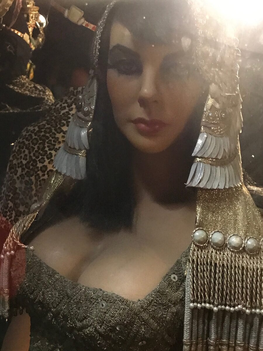 A lifelike mannequin dressed as Cleopatra with dramatic makeup, ornate headdress, and a beaded gold outfit, illuminated by warm light.