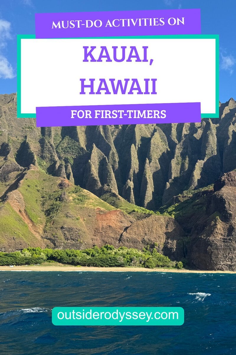 Steep green cliffs rise above the blue ocean under a clear sky, with colorful banners reading Must-Do Activities and Things to Do on Kauai, Hawaii for First-Timers and a website link: outsiderodyssey.com.